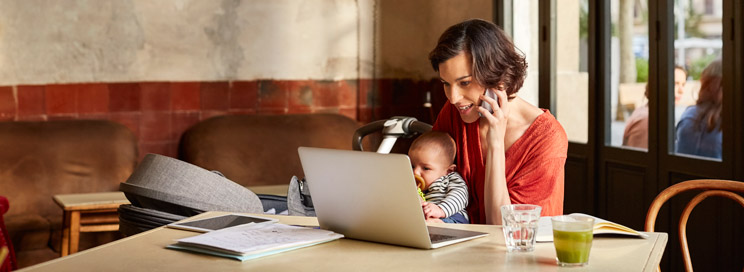Woman with baby on phone with laptop working